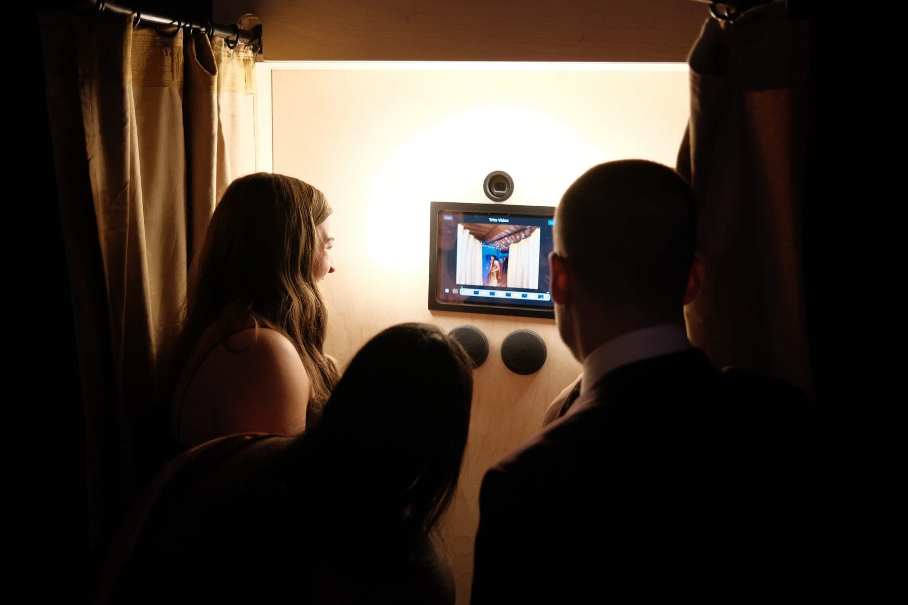 Guests gathered around the booth screen watching a playback
